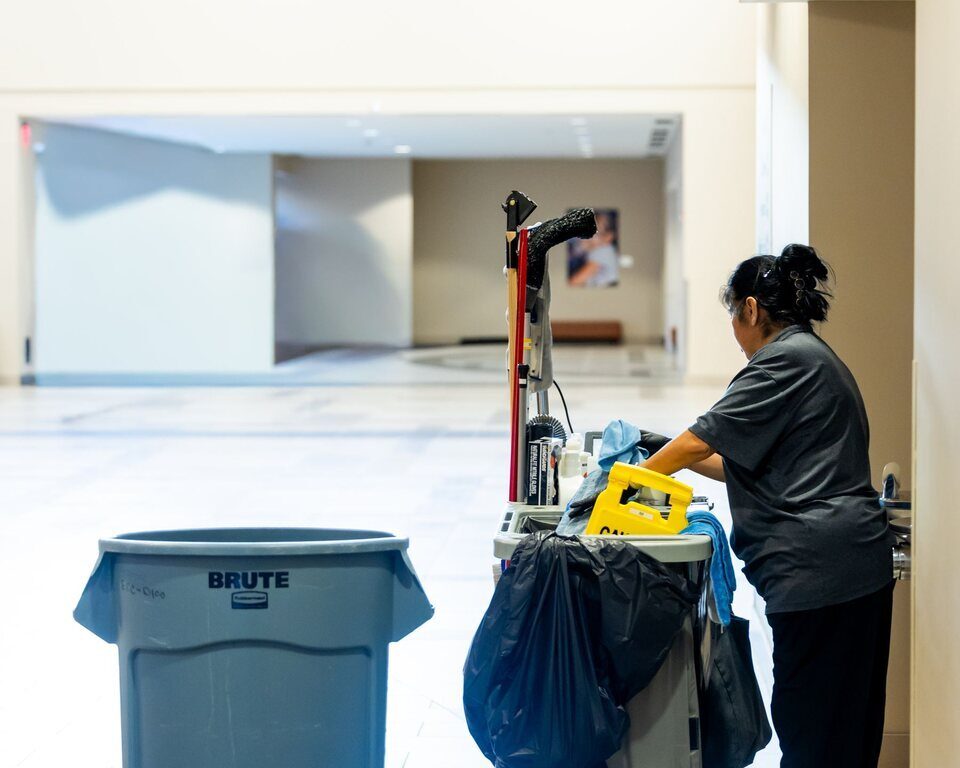 An ACC Services team member moving a stocked janitorial cart through a clean commercial corridor